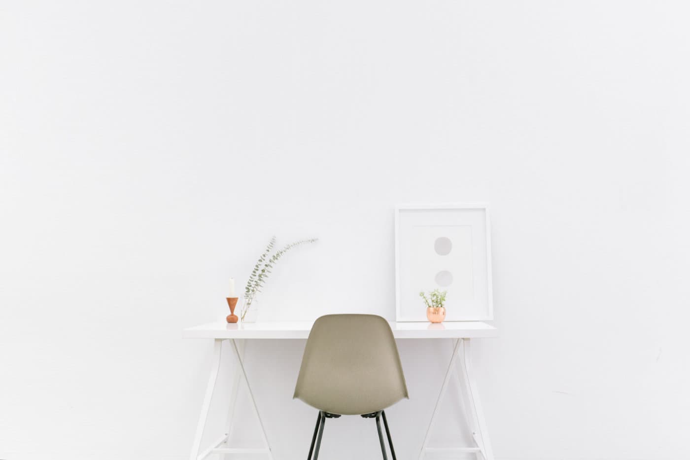 A very clean white room with a small table and a chair in front of it. It's very minimalistic.
